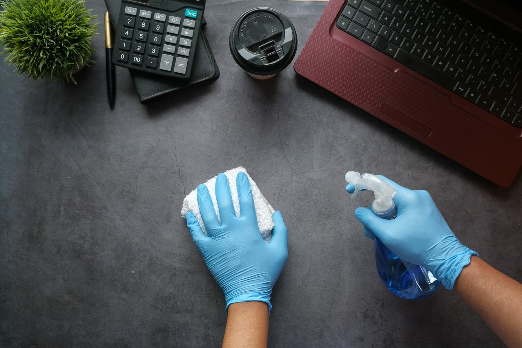 Gloved hand disinfecting a laptop keyboard